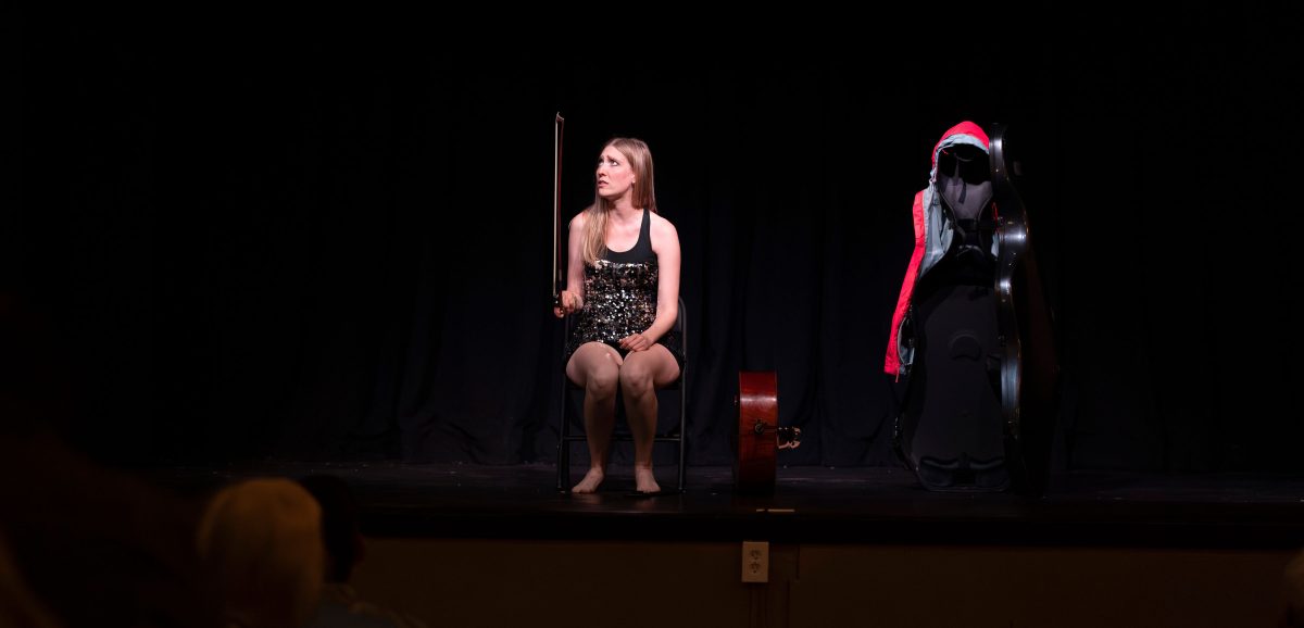 A woman sitting and holding a violin bow on a stage