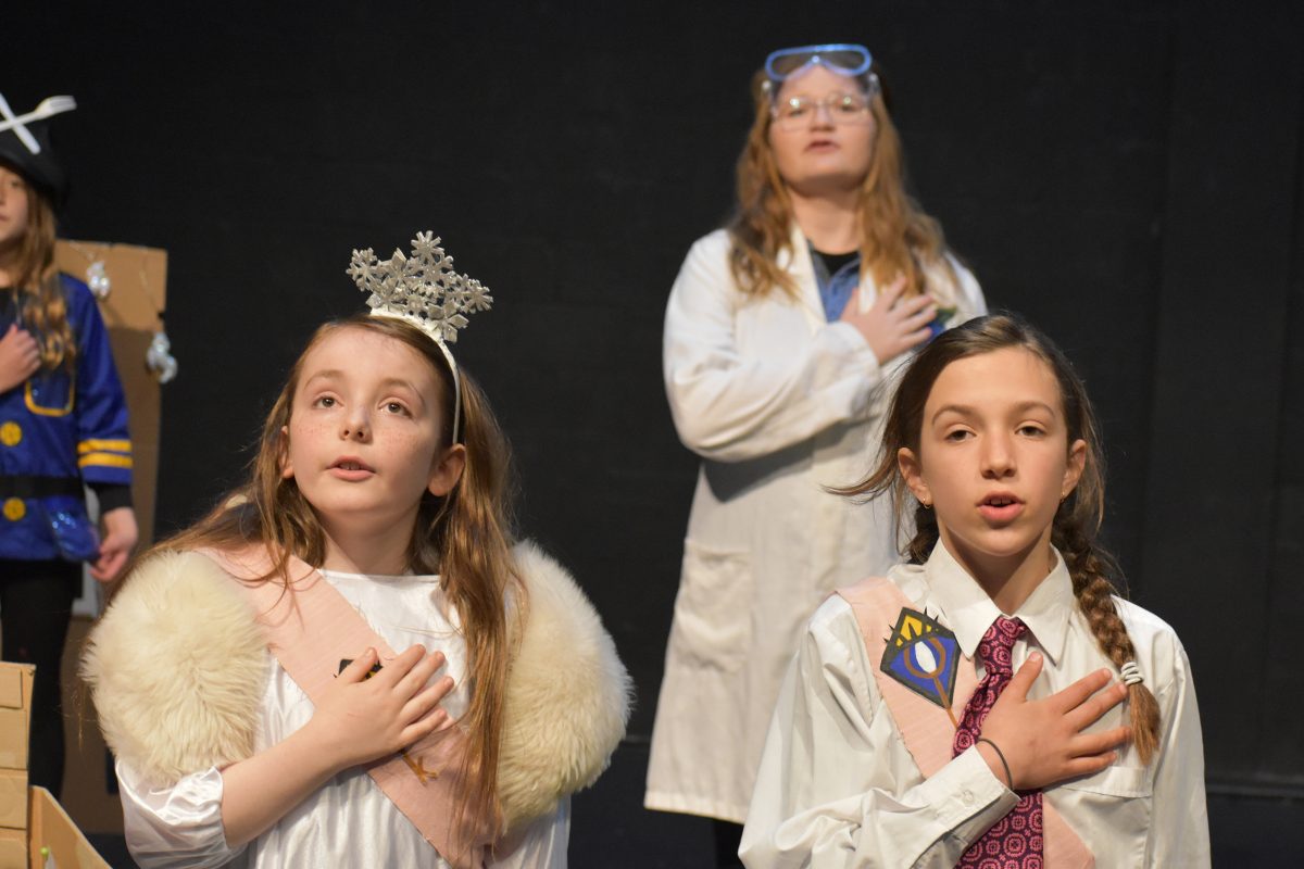 Three kids in costumes with their hand on their heart