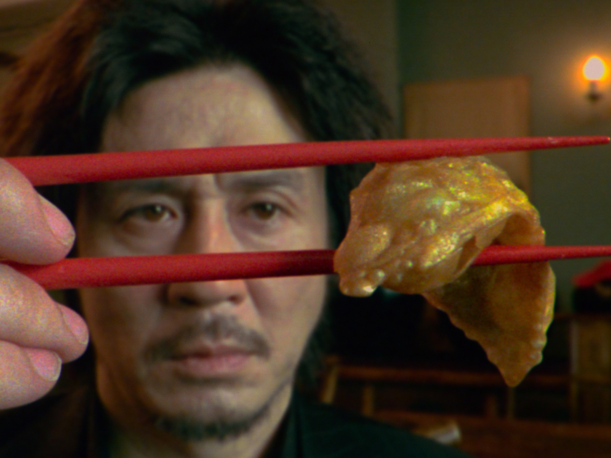 Still from Oldboy showing a man holding a fried dumpling between red chopsticks