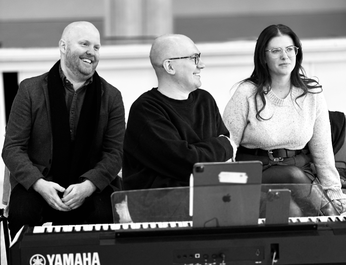 A black and white photo of three people sitting behind keyboard, smiling