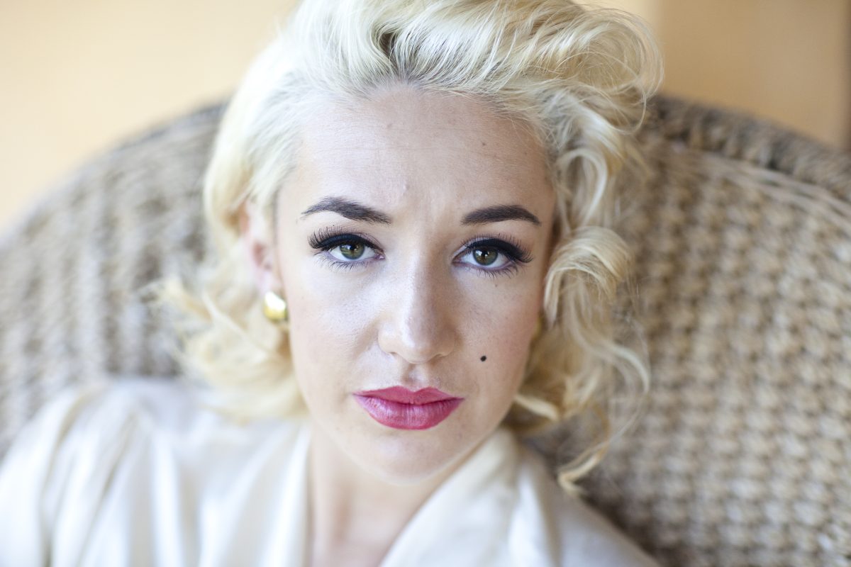 A close-up photo of a woman with blonde hair, heavy eyeliner and red lipstick