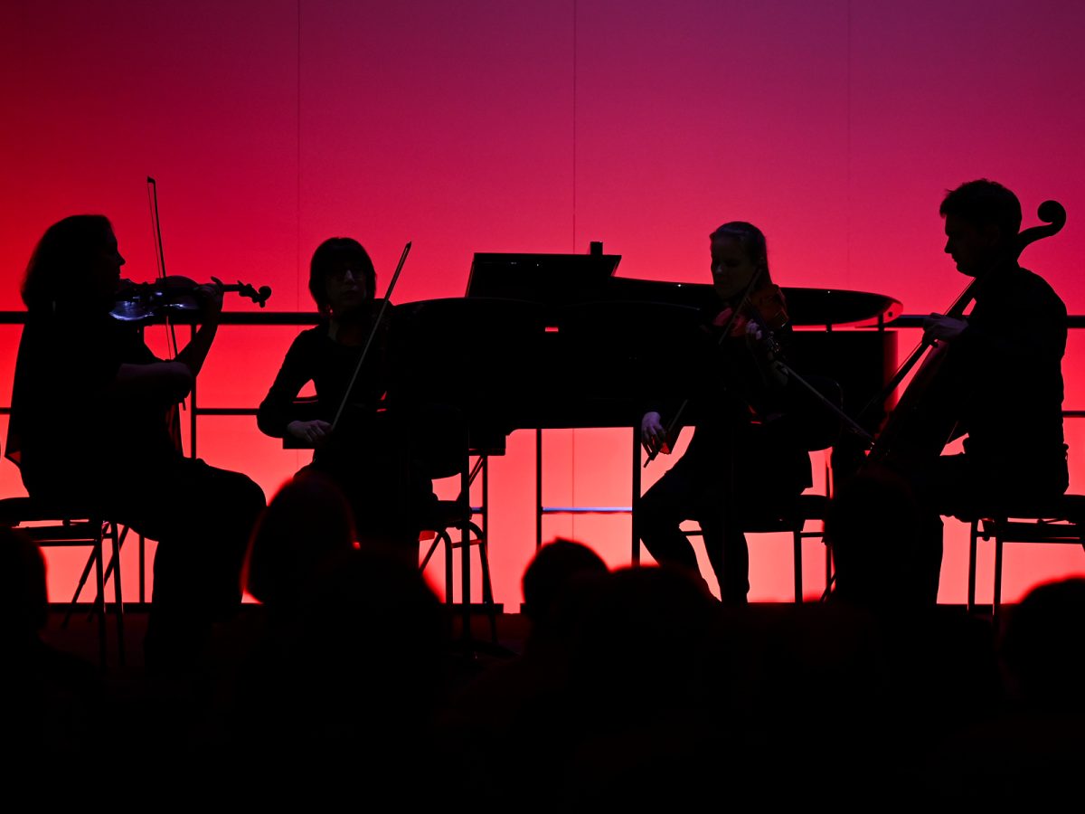 A silhouetted string quartet plays against a vibrant red backdrop.