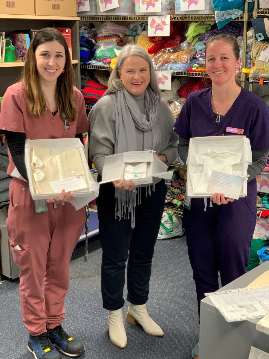 Three women holding boxes of baby dresses