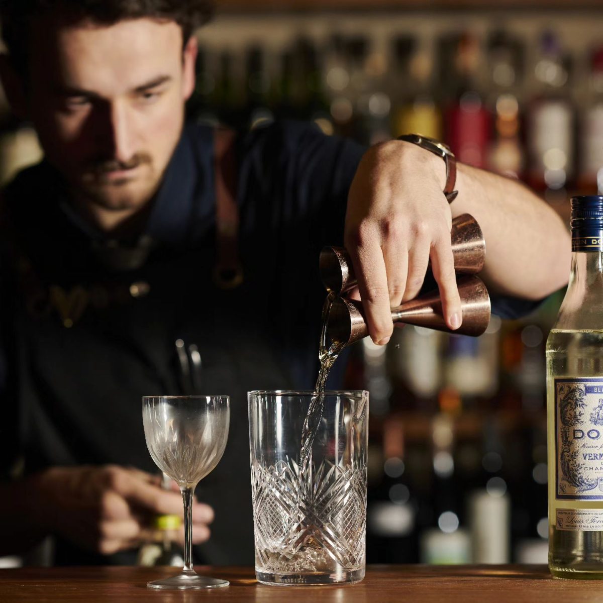 A bartender pours two measures of spirit into a glass