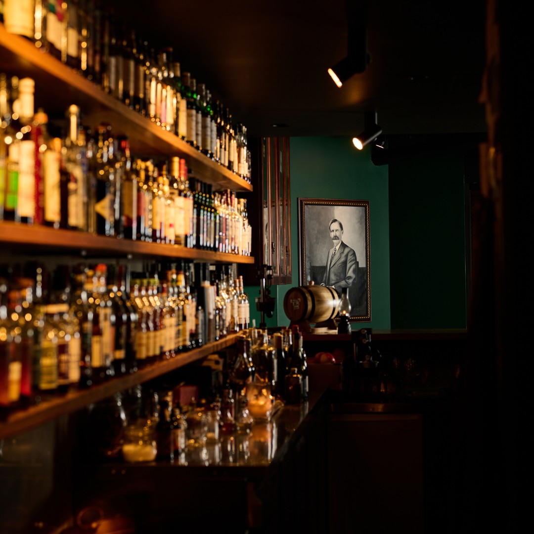 Interior of green-walled bar with many whisky bottles and a black-and-white vintage portrait 