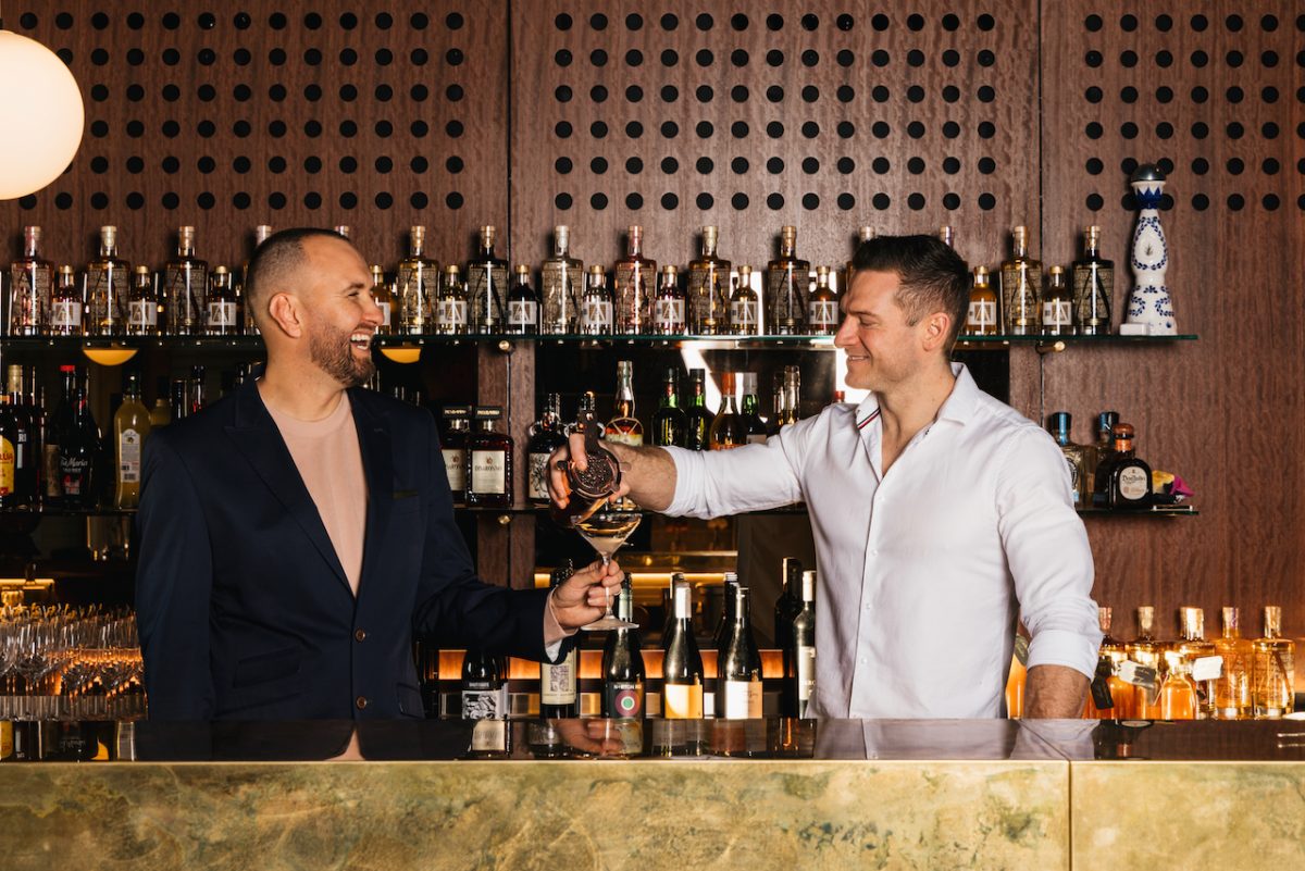 A man in a white shirt pours a cocktail for a man in a black shirt