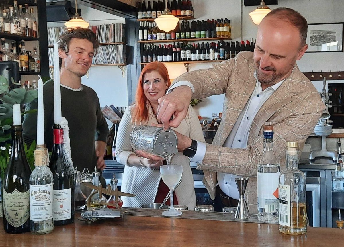 a man and a woman watching a man pour a cocktail