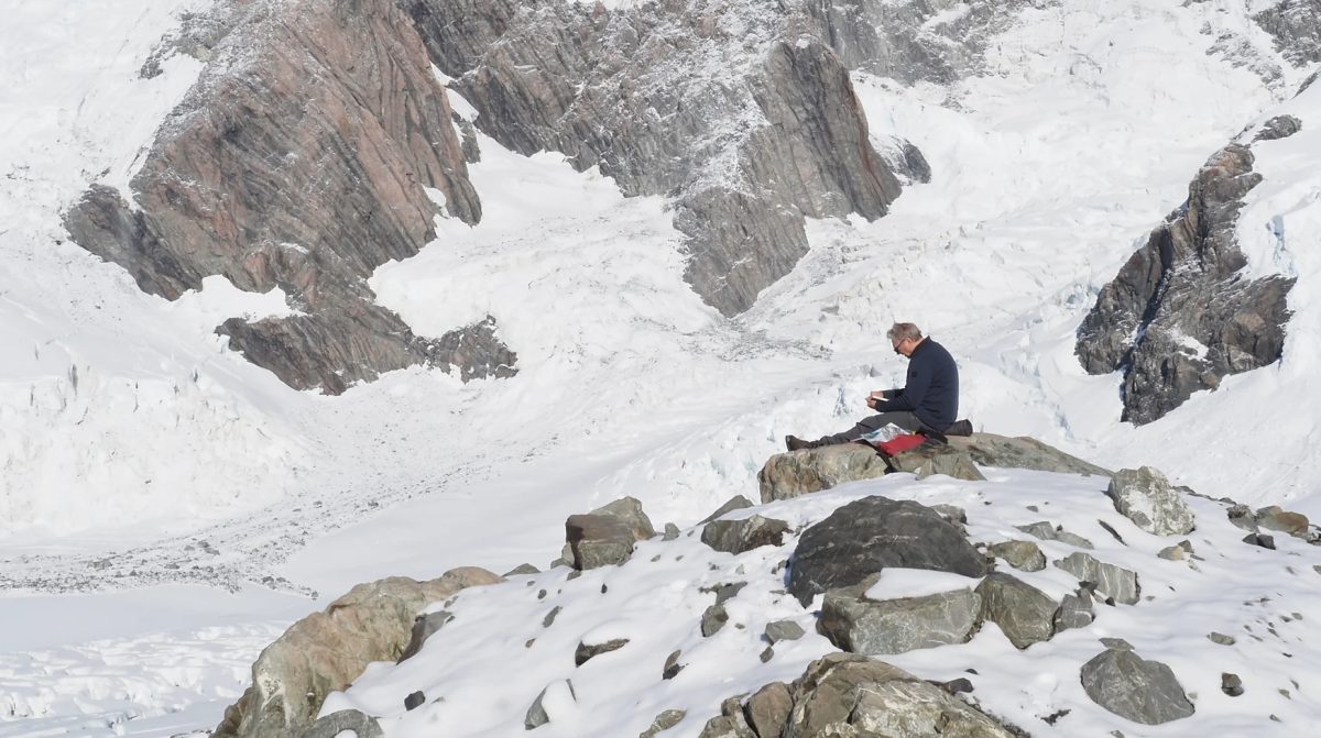 Photograph of an artist seated and painting on a rock