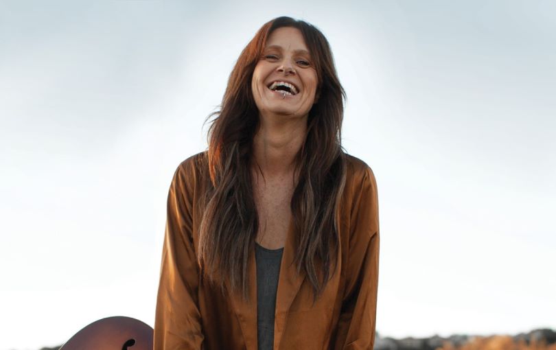 A photograph of a smiling woman with a guitar.