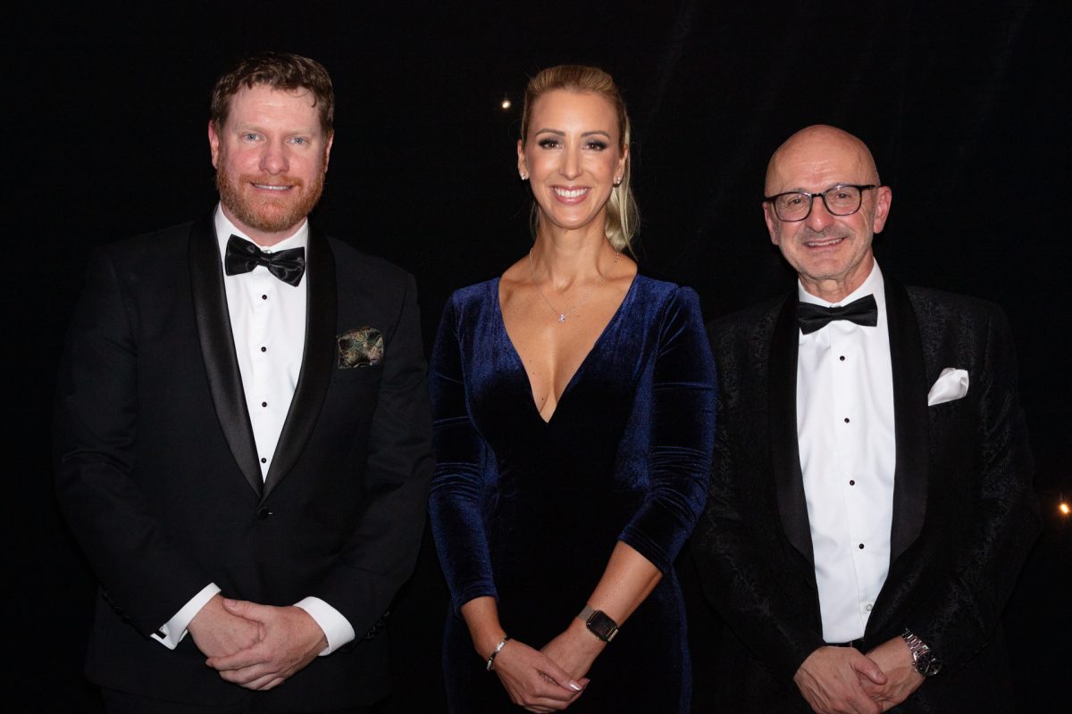 Three people standing in front of black background.