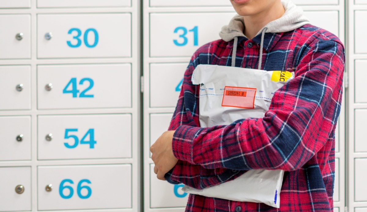 young man holding parcel in front of parcel lockers