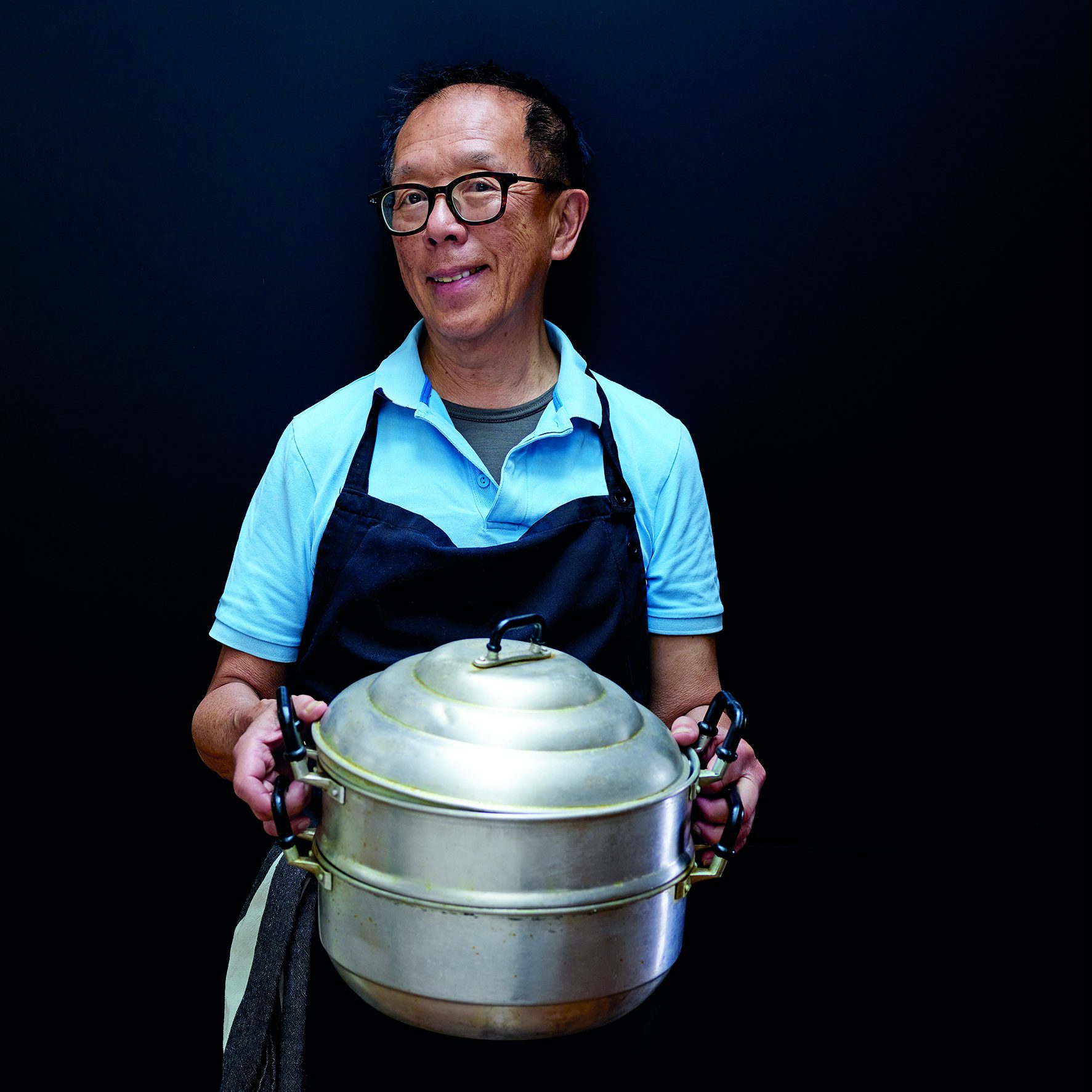 Image of older Asian man holding a large steamer pot.