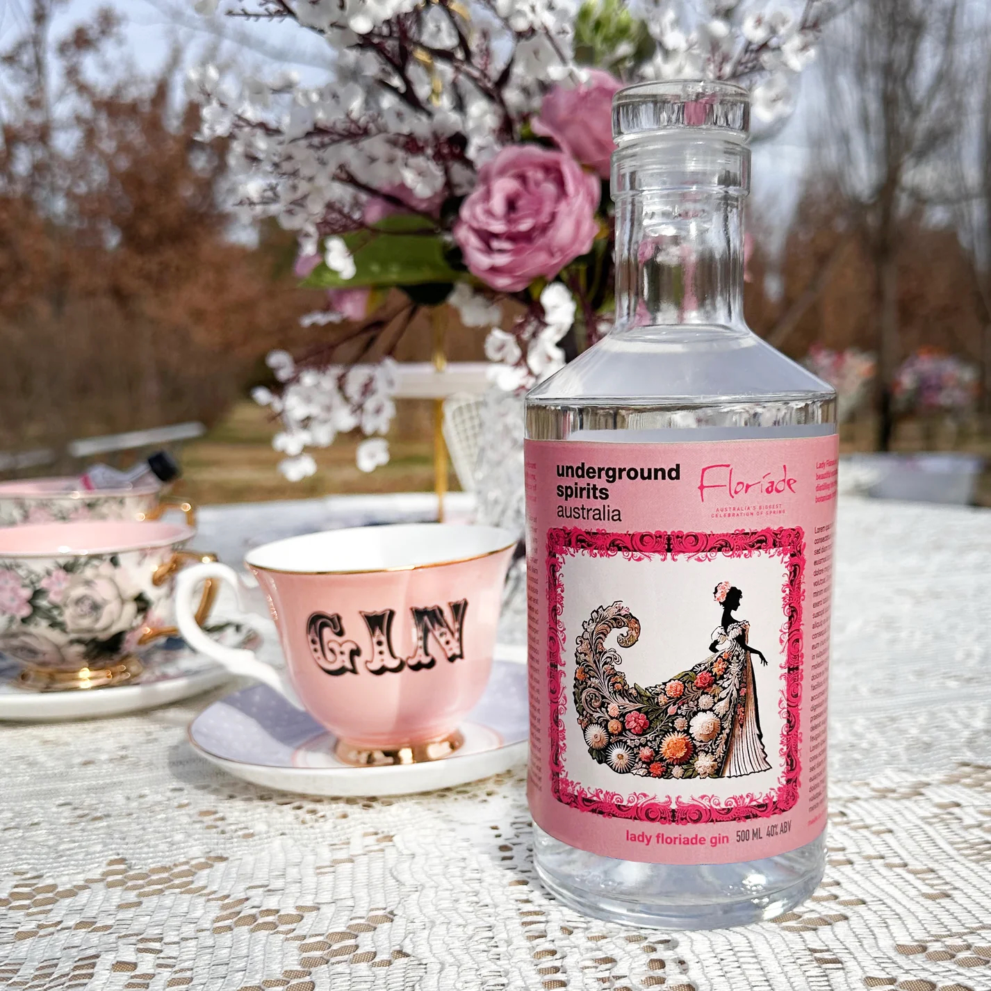 A pink teacup that reads 'Gin' in stylised text and a pink bottle of Underground Spirits Lady Floriade Gin featuring an image of a woman in Regency style floral dress.