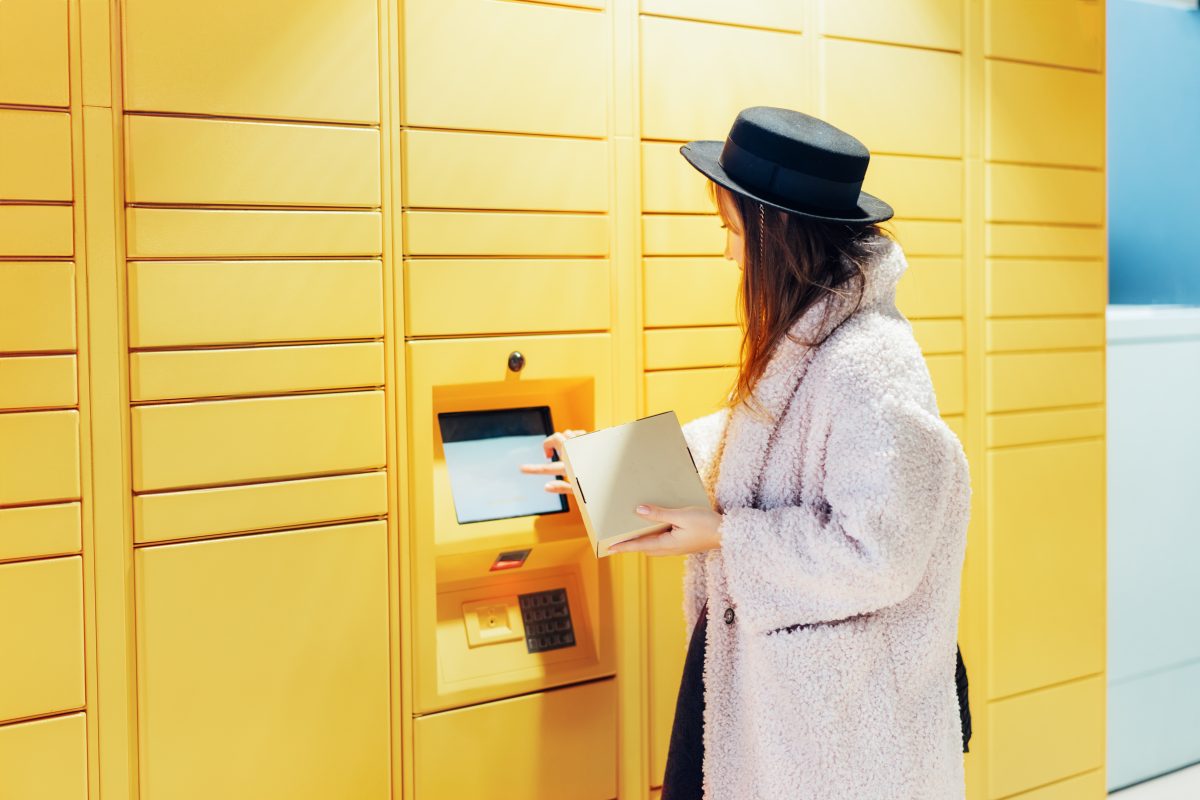 woman with box using modern postal automatic mail terminal with self service device for pickup of an order