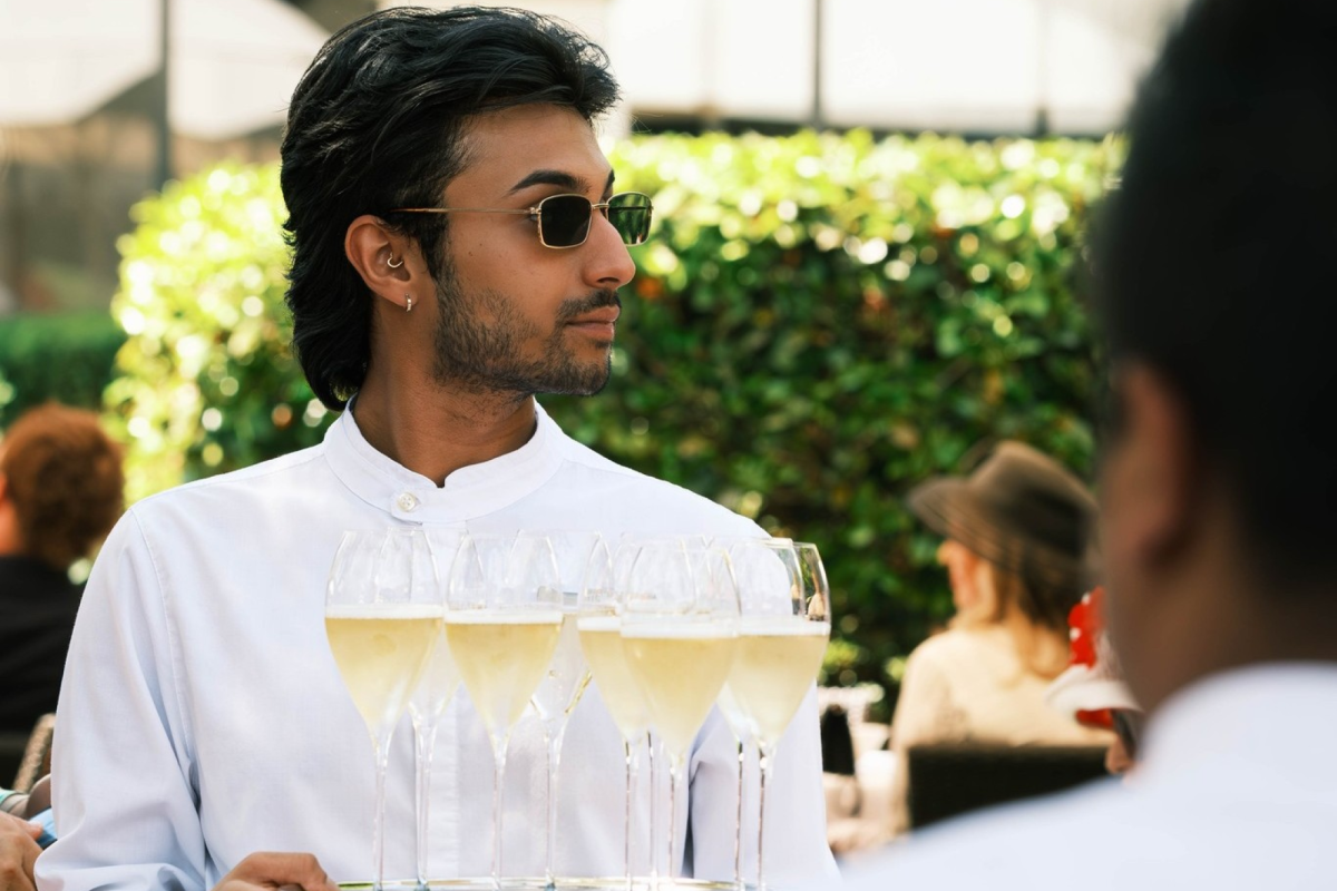 a waiter wearing sunglasses and a white shirt holding a tray of champagne glasses filled with champagne