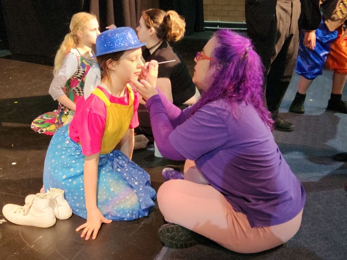 A woman applying make-up to a child's face, who is in costume