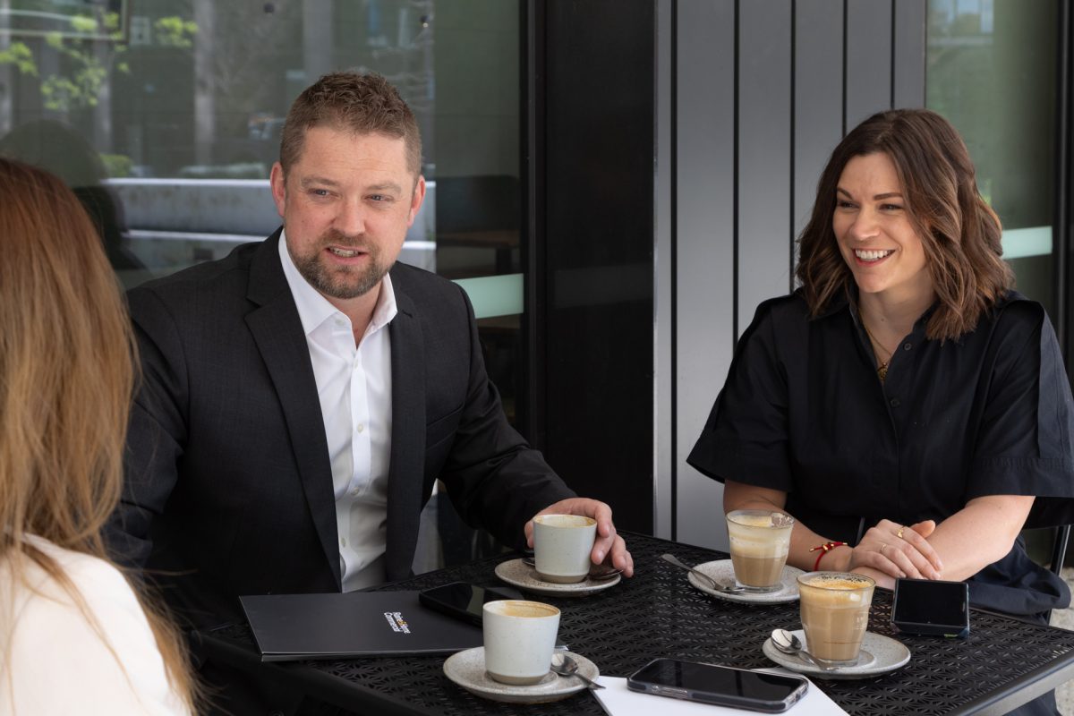 three people sitting at a coffee table outside having a discussion