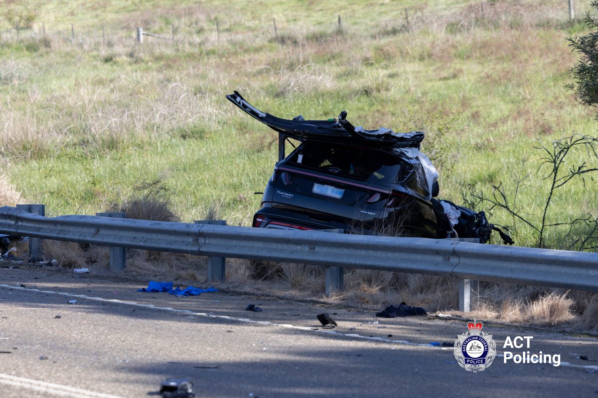 A mangled black car at the side of the road