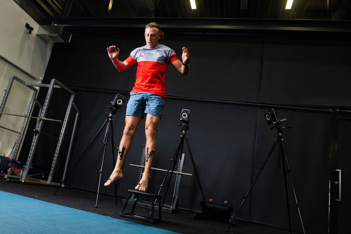 A young man jumps off the floor to measure his vertical jump height using measuring equipment. 