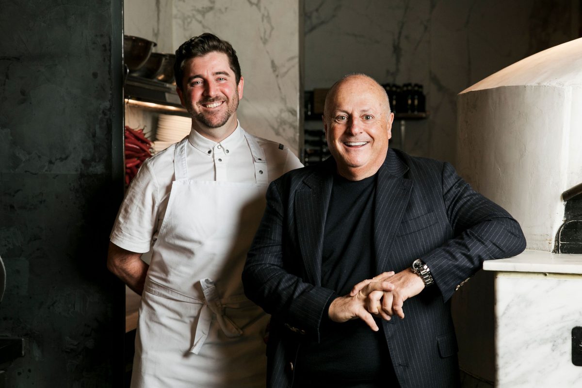 A man in white chefs uniform and a man in a black suit.