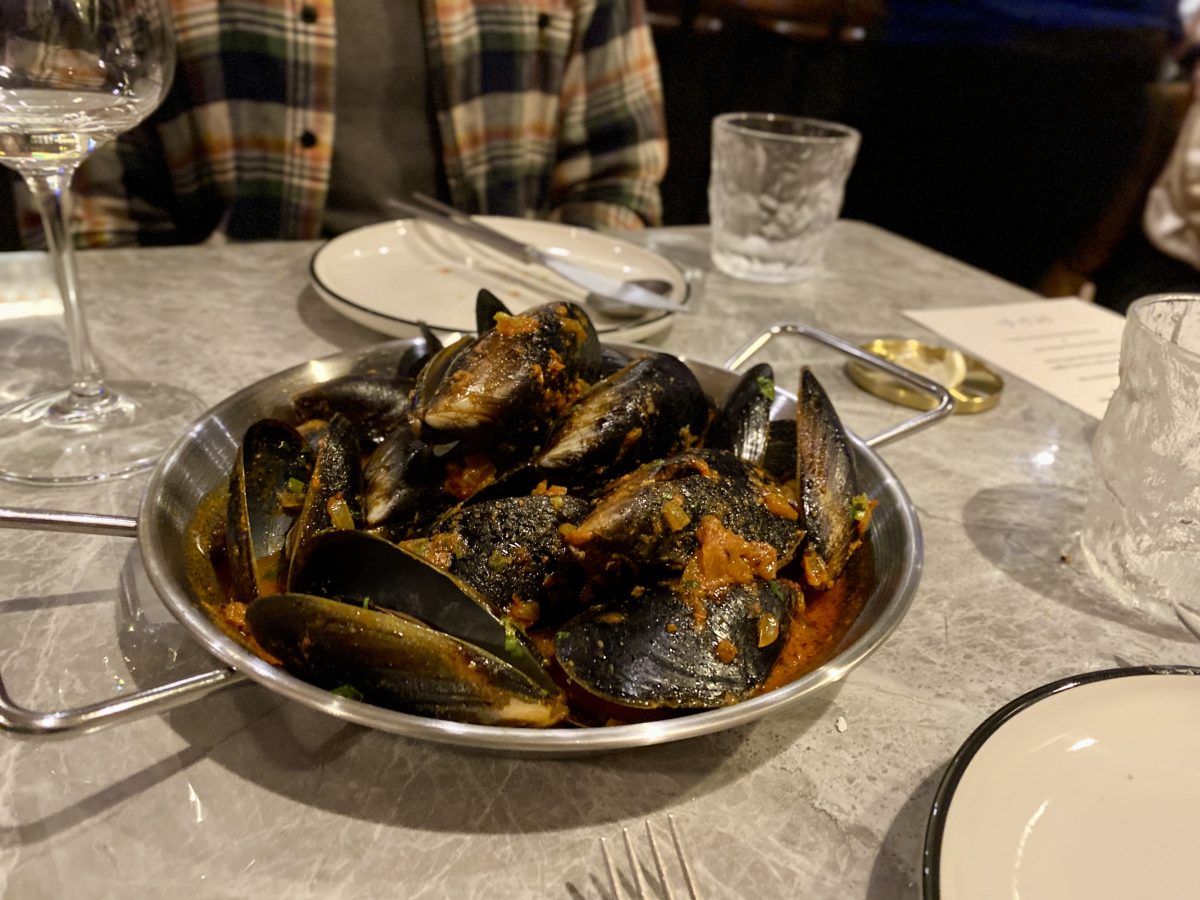 Metal dish filed with black mussels in a tomato sauce.