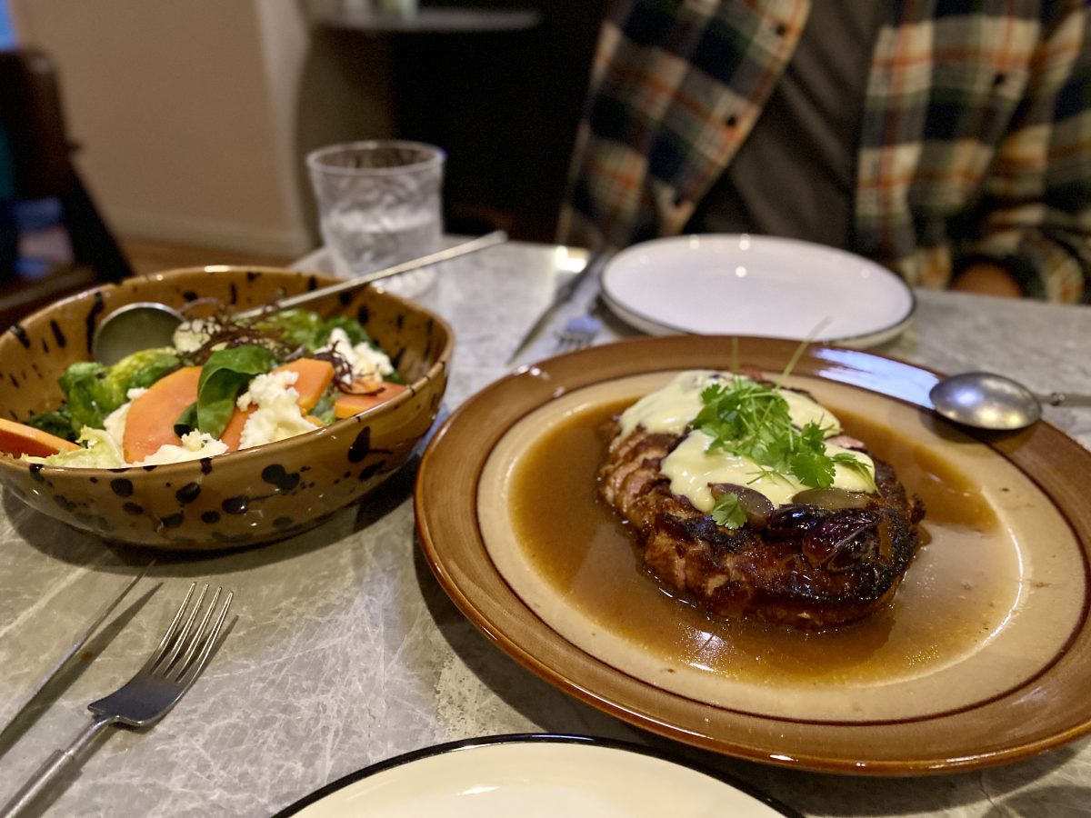 A retro brown plate with sliced pork covered in mayonnaise and topped with herbs, and a brown spotted salad bowl on the side. 