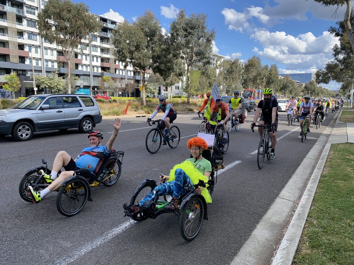 Two recumbent bicycle riders wave as they lead a group of cyclists down the road.