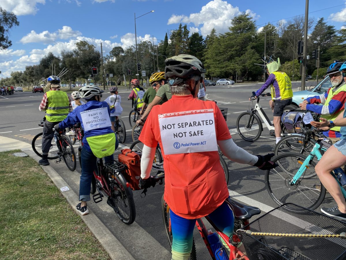 A cyclist in a group wears a sign that reads 'not separated not safe' as part of a protest ride.