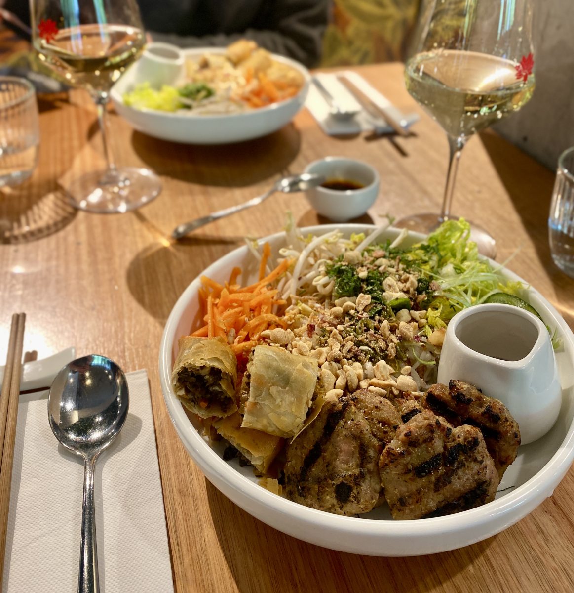 A bowl of salad, noodles, meat patties and a chopped spring rolls.