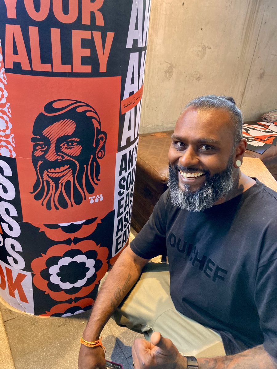 AK smiles next to a red and black print depicting his face.