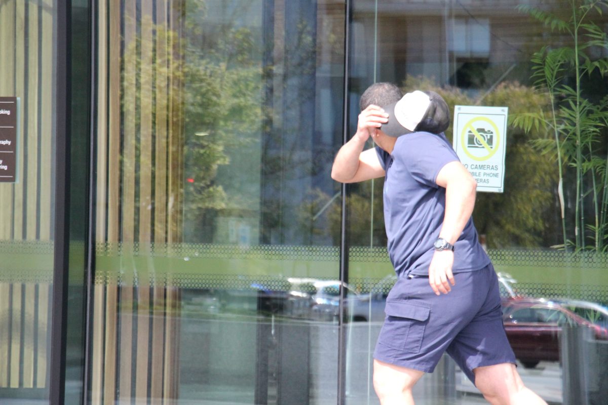 A man in a navy shirt and shorts covering his face while running