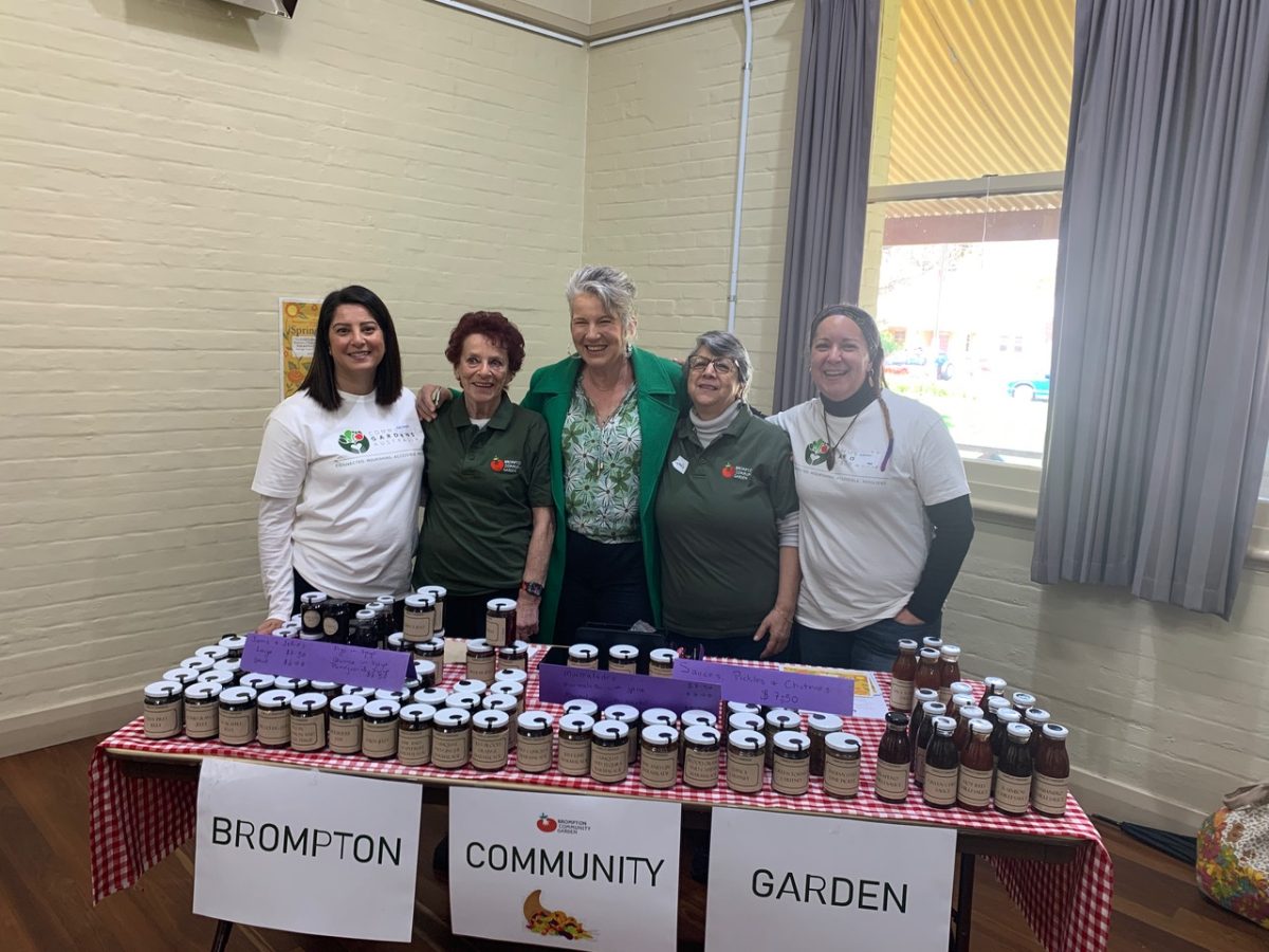 A group of women pose behind a table of jams and preserves.