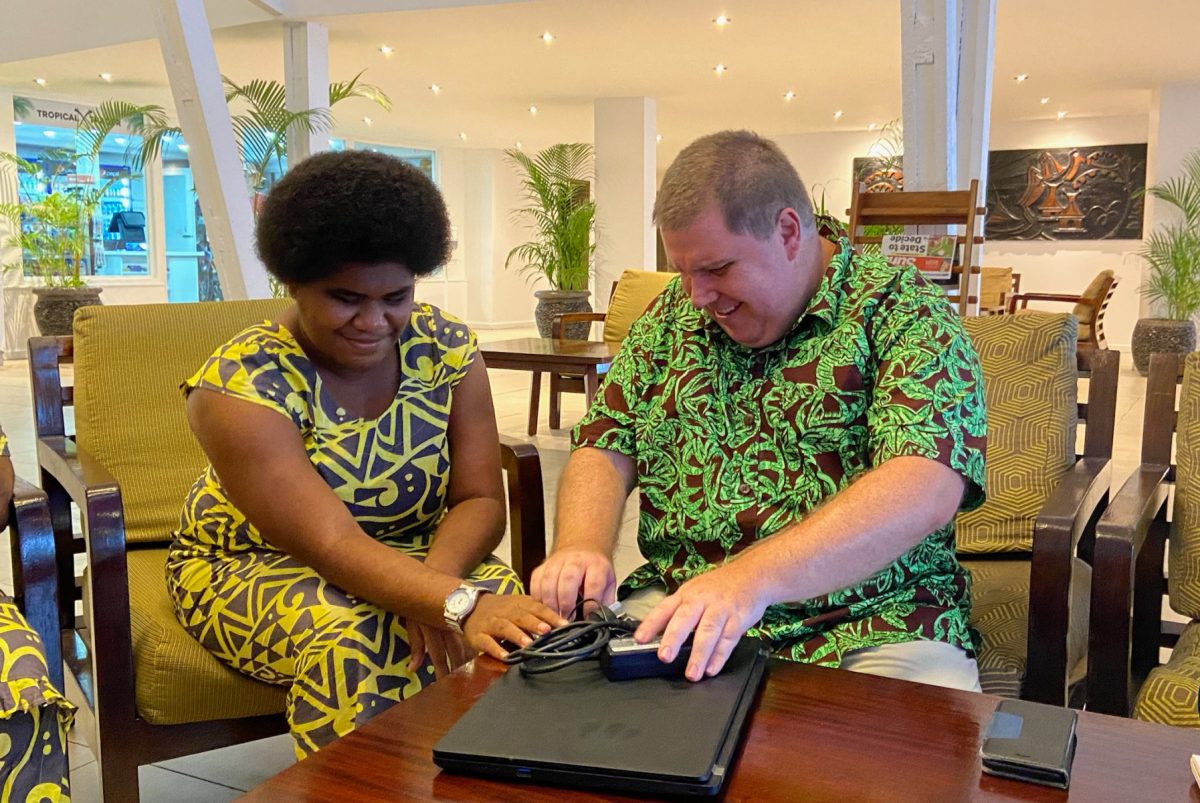 Ben and Naomi sitting together and smiling while touching a laptop.