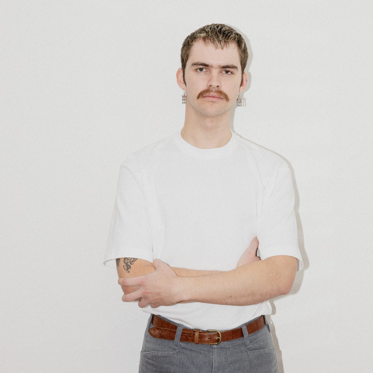 Person with mustache crosses their arms and poses seriously