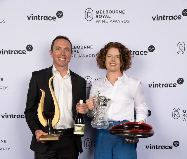 A man and woman hold several trophies and pose for the camera.