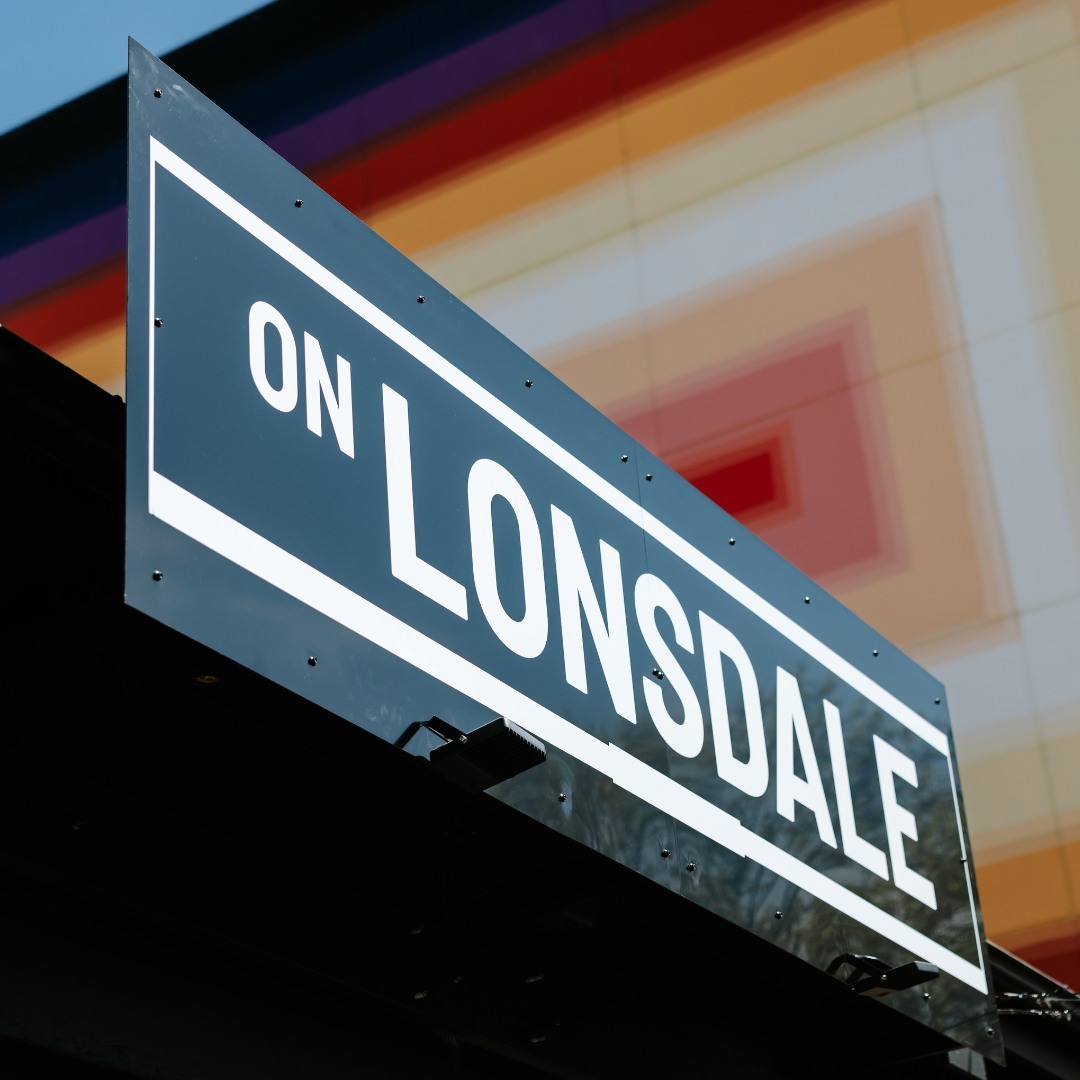 A black and white sign reading On Lonsdale with a red, orange and white mural in the background.