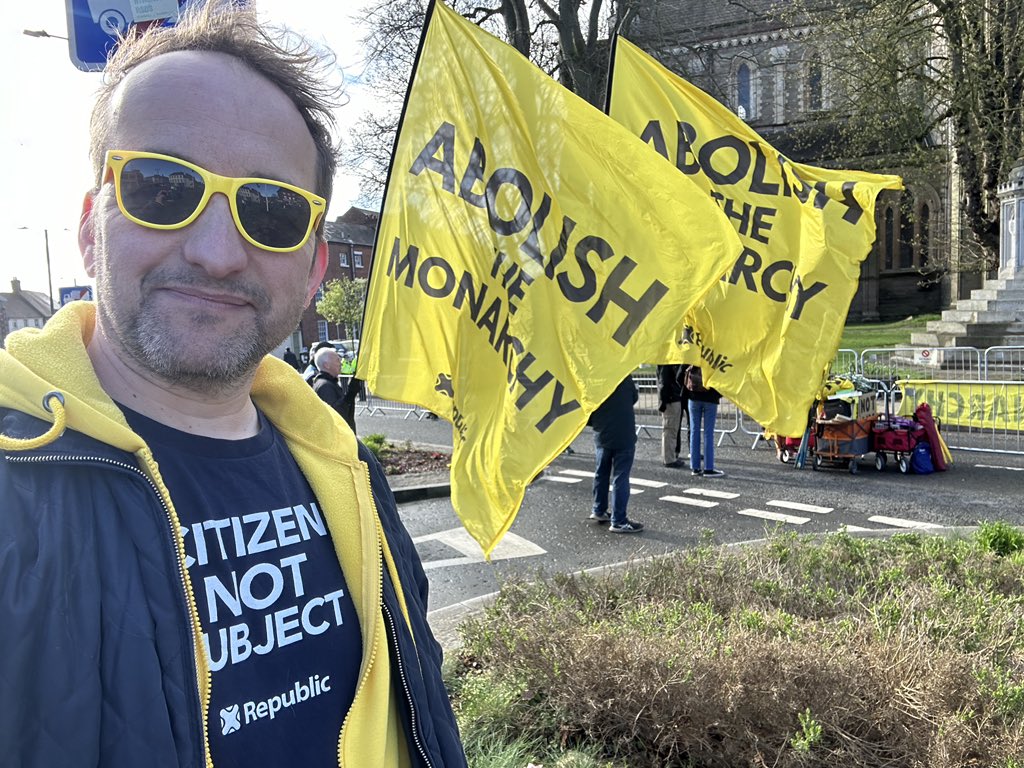 Graham Smith standing in front of two big 'Abolish the Monarchy' flags in the UK.