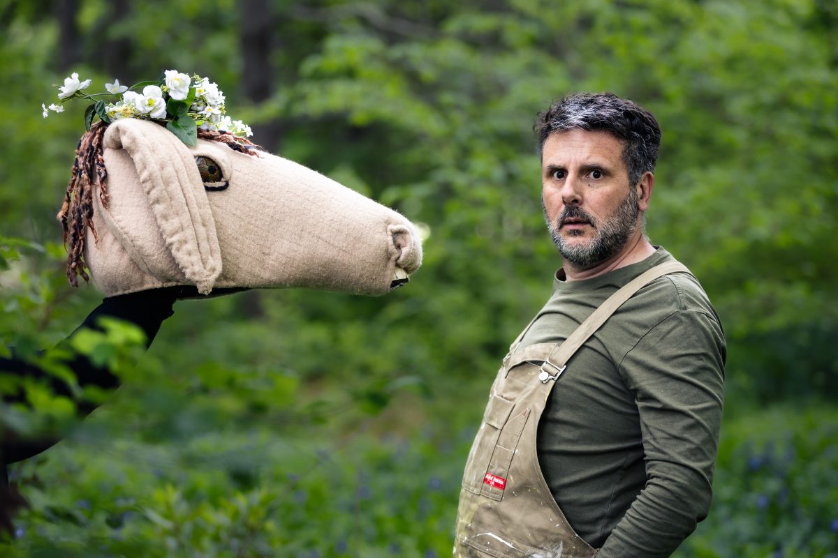 a mand standing next to a hand puppet surrounded by green bushes