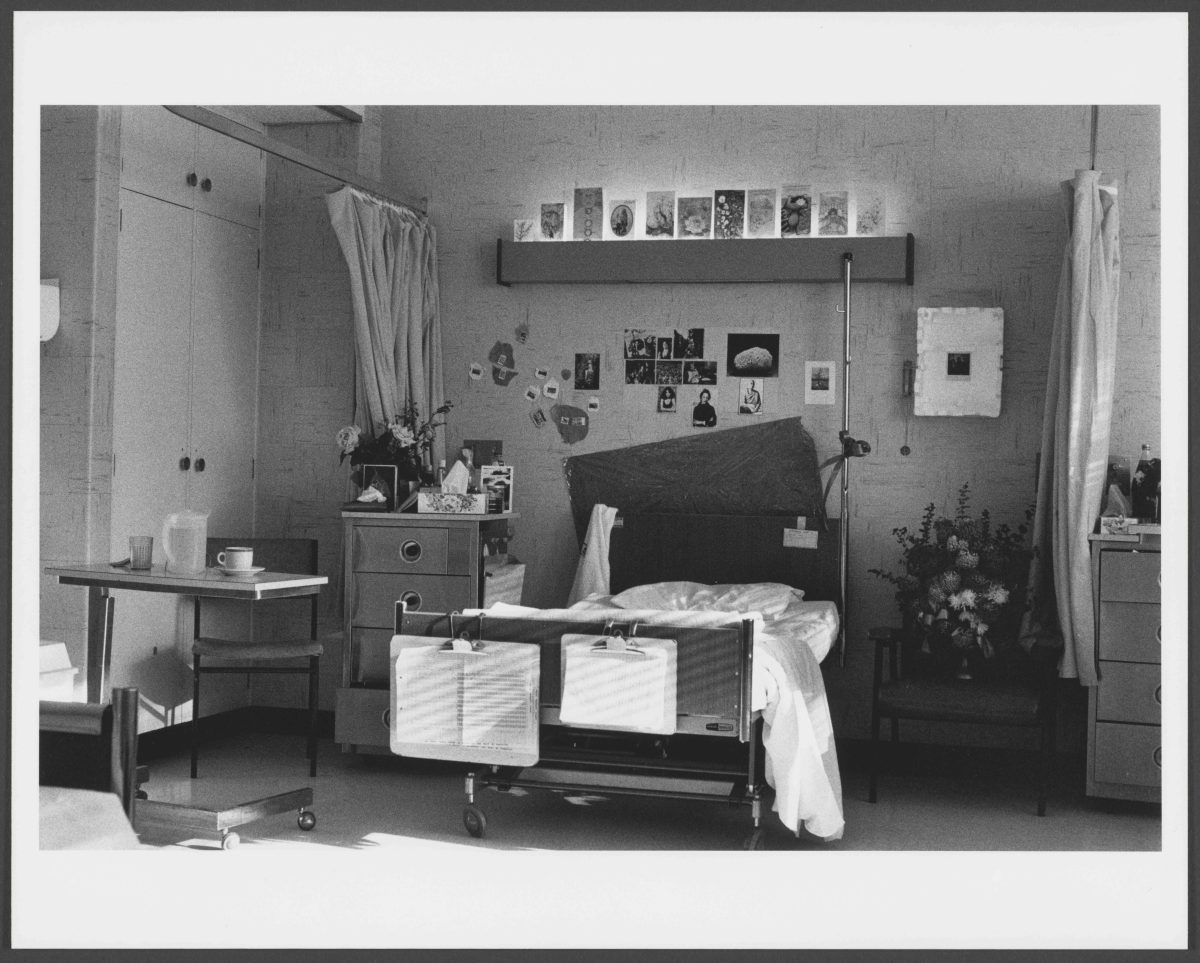 A deserted hospital bed with photographs on the back wall