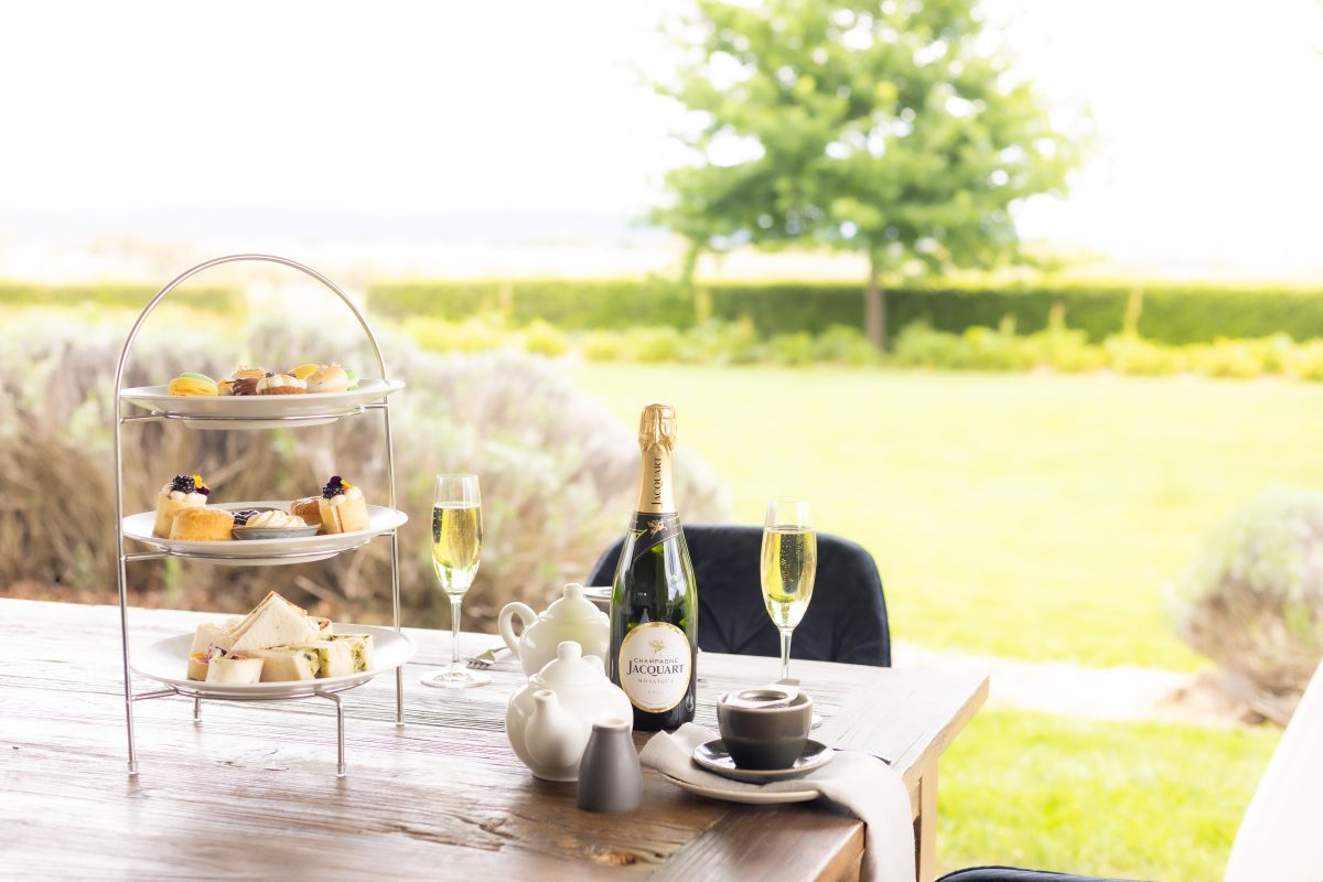 A table with a three-tiered high tea display, teapots and bottle of champagne.