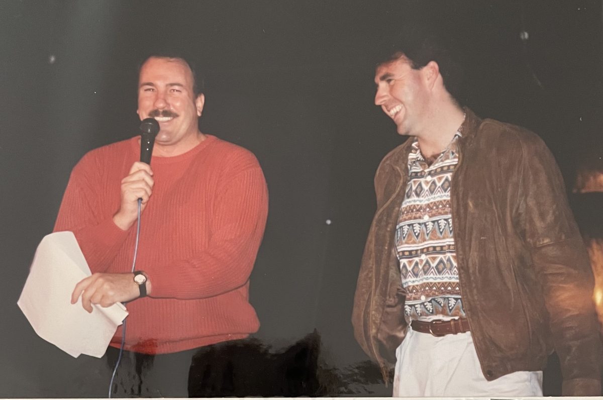 two smiling men, one with a mic