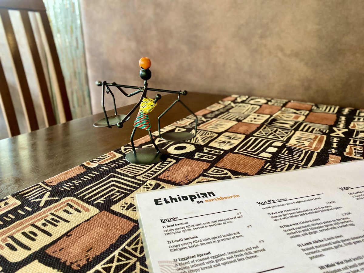 A small wire figurine and menu sitting on a patterned cloth.