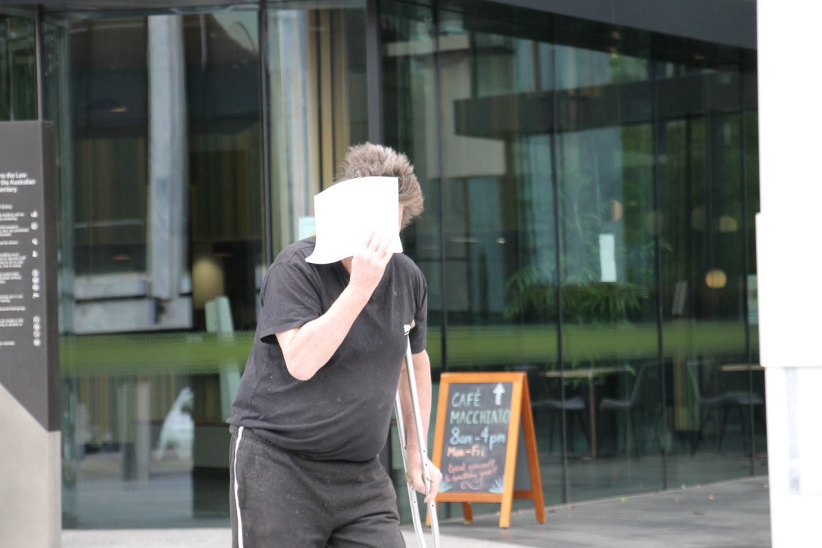 A man holding a crutch with one hand and holding a paper to cover his face with the other