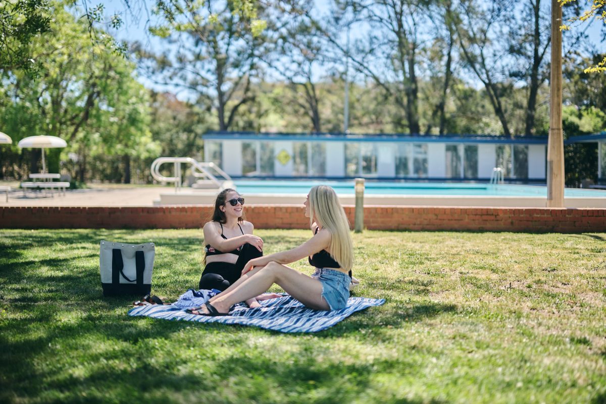 two women relaxing on the grass at a public pool