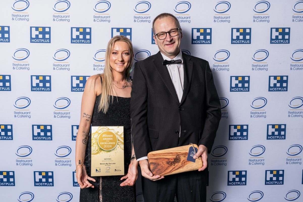 Two people smile and hold up awards