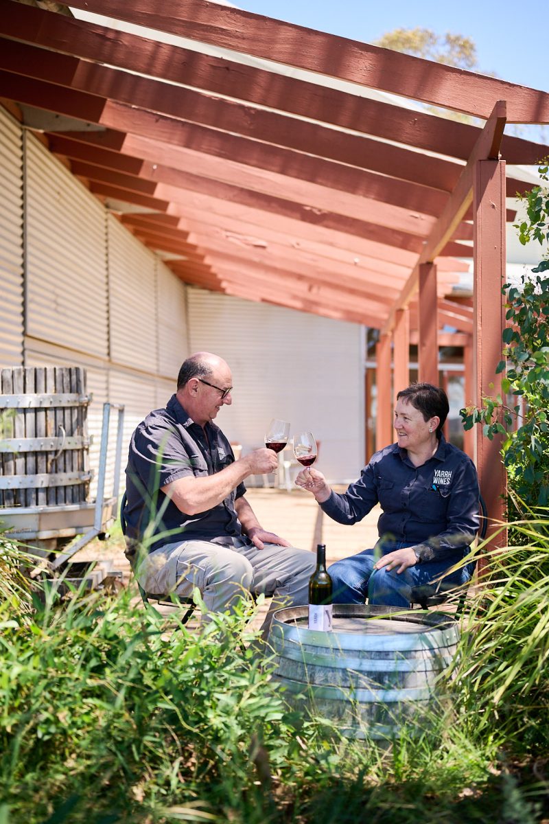 A man and woman sit outside and 'cheers' their wine glasses together