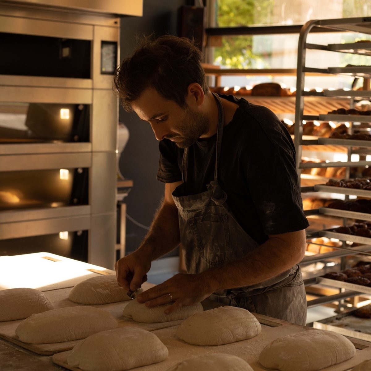 A man scores loaves of bread on a bench.