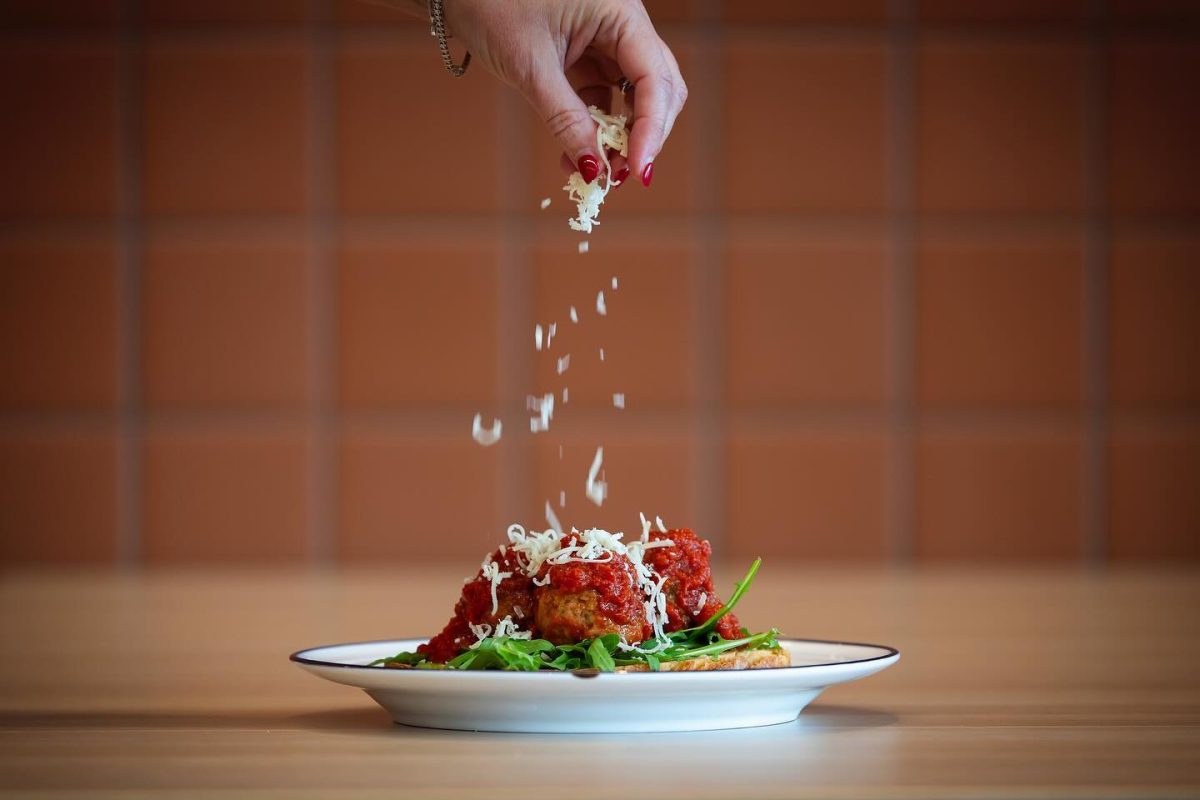 A hand sprinkling cheese onto a plate of meatballs