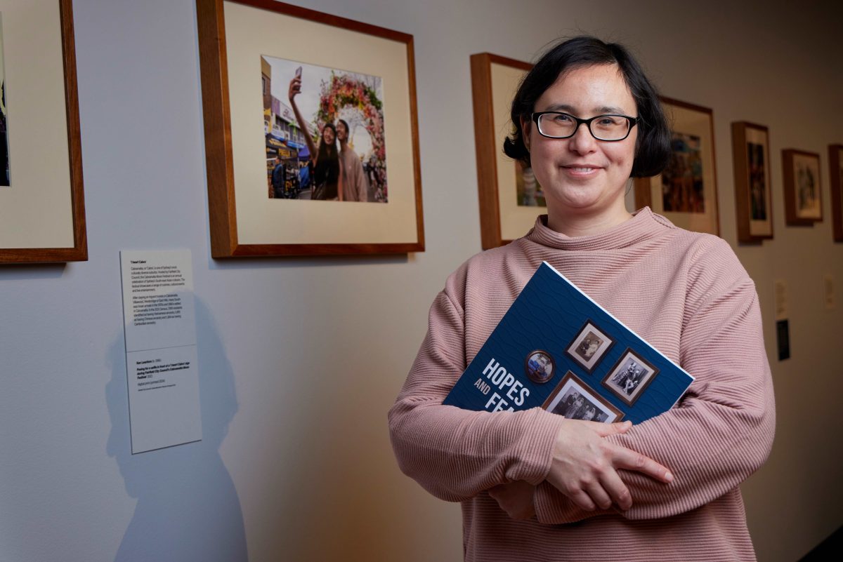 A woman in front of exhibition photo frames while holding the Hopes and Fears exhibition book.