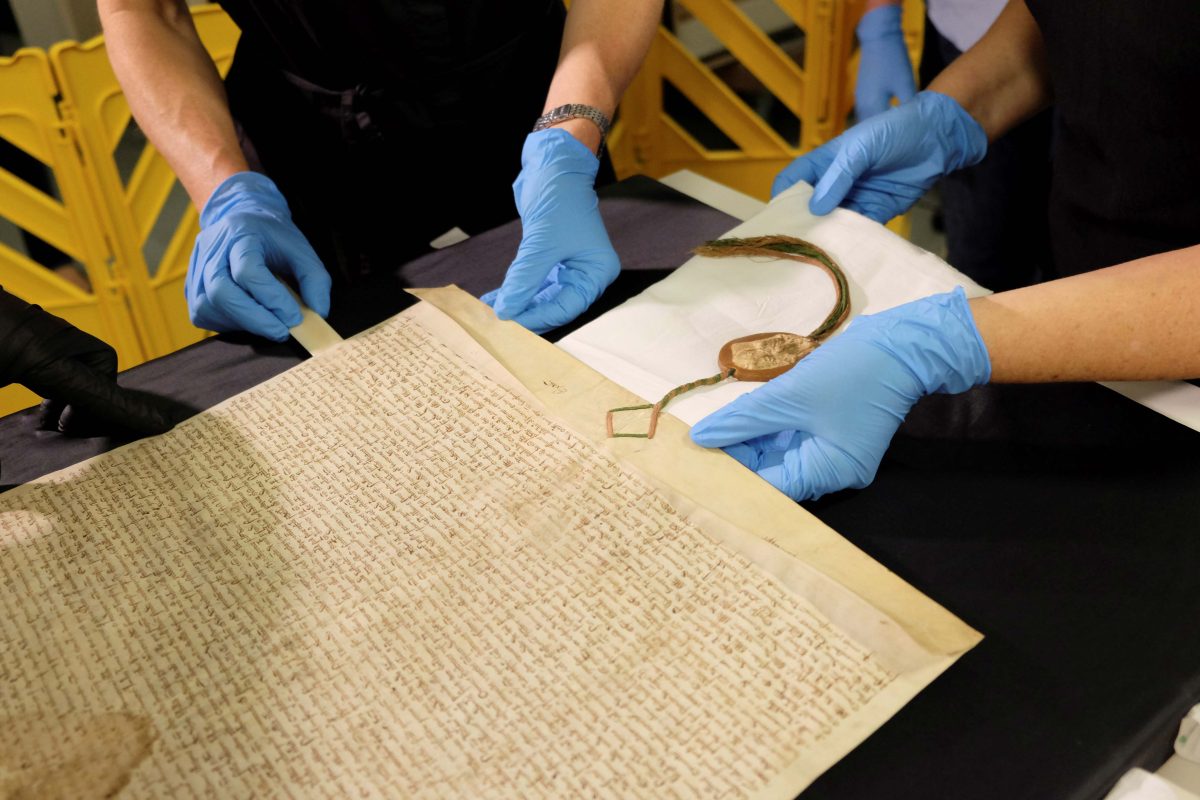 Blue-gloved hands work on ancient document